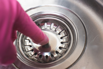Man in pink glove plugs cork in sink for dishwashing. Save water