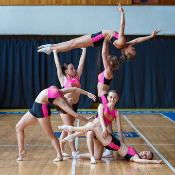 cheerleader group perform trick, smiling beautiful girls in black and pink sportswear shows off their moves, dancers hold the girl in their arms