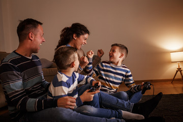 Parents with the children sitting at home on a pleasant evening and playing games on console. They challenge each other to win.	