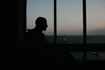 A stylish bald man sits with his smartphone aboard a ship. Silhouette portrait.