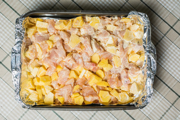 Pickled pieces of chicken fillet with potatoes in baking tray in oven.