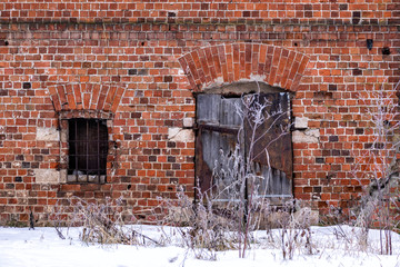 Red brick facade abandoned building. Wooden door, barred window. Front view