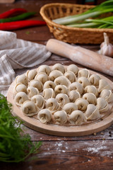 Russian national cuisine. Raw meat dumplings laid out on a cutting board with vegetables, herbs and specs on a flour-sprinkled wooden table.