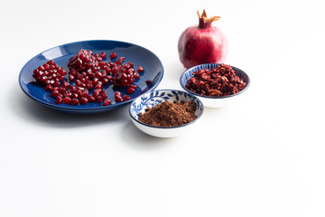 ground pomegranate seeds spice  in bowl close-up on white background with garnet fruit and berries