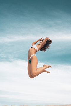 Young woman in bikini jumping over sand