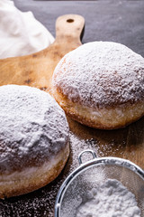 Donuts covered with powdered sugar on the wooden cutting board and stony worktop.