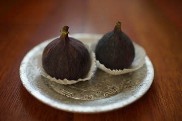 Two ripe sweet figs in silver plate on a wooden table.
