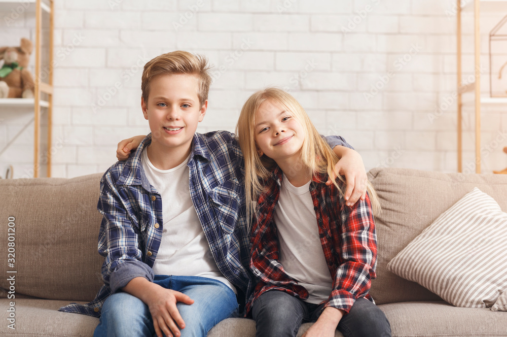 Wall mural Brother And Sister Embracing Smiling Sitting On Couch At Home