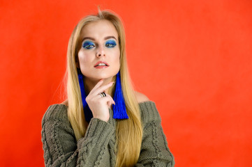 Nice girl model blonde with long hair and excellent make-up is standing in front of the camera on a red background in a green sweater. A woman shows different emotions.