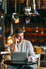 Middle-aged man working on a laptop computer, sitting at the cafeteria, lifestyle concept
