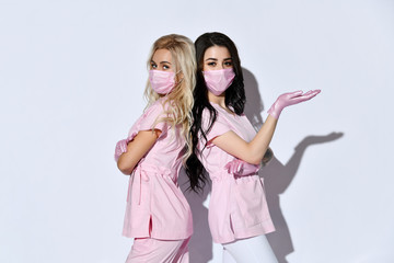 Two ladies in pink scrubs, disposable gloves and medical masks posing isolated on white. Medical...