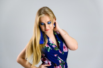 Nice girl with fluttering hair and great make-up in front of the camera on a white background in a multi-colored dress. Model stands in different poses.