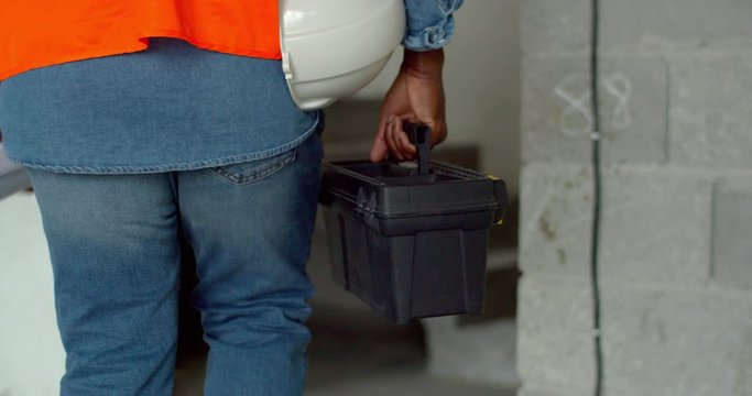 Close up of the box with tools for constructor in hand of African American man. Male builder carrying a drawer while walking at the building.