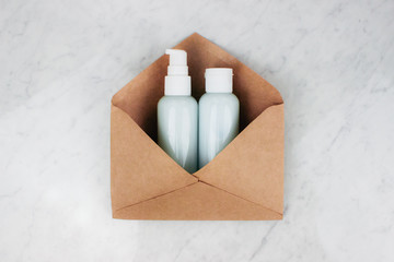 Cosmetic plastic bottles with cosmetic product shampoo, gel, lotion, cream for skin in craft envelope on marble background top view copy space. Cosmetic containers kit. Banner template. Stock photo.