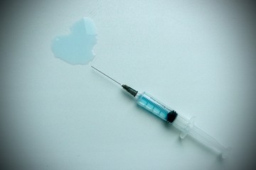 a medical syringe from which a blue liquid is poured in the form of a heart. White background,...