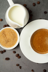 black coffee in a white cup, milk and brown sugar on a black background