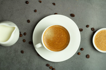 cup of black coffee, milk jug and coffee beans on black background close-up