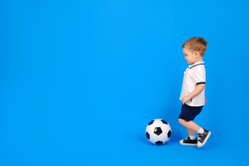 Little kid in white football jersey kicking a football on blue background