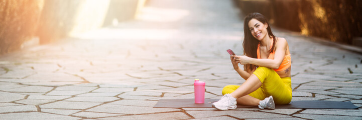 Young attractive fitness model listening music on smart phone charching positive energy before workout outside