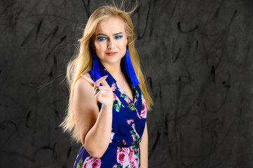 Fototapeta premium The model stands in different poses. Nice girl with flying hair and excellent make-up in front of the camera on a gray background in a multi-colored dress.