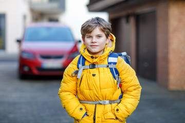 Little school kid boy of elementary class walking to school. Portrait of happy child on the street with traffic. Student with in yellow jacket and backpack in colorful winter clothes.