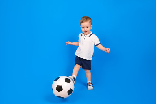Little kid in white football jersey kicking a football on blue background