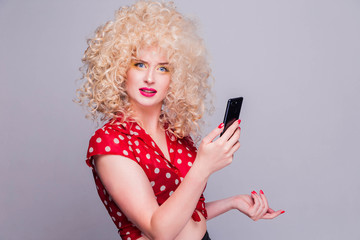 Beautiful blonde girl with a curly curly hairstyle, bright yellow make-up and red polka dot blouse  looks at camera with pensive expression