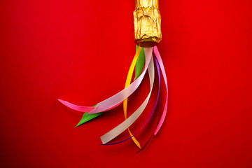 Champagne bottle neck in gold foil and colorful colored satin ribbons on bright pink background,...