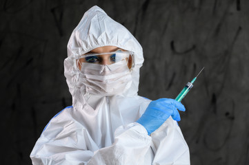 A doctor in a protective white suit with a syringe in his hands and blue rubber gloves stands in different poses on a gray background.