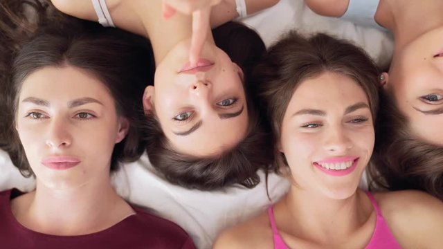 Happy female friends lying head to head on bed at hen party