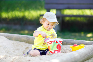 Cute toddler girl playing in sand on outdoor playground. Beautiful baby having fun on sunny warm...