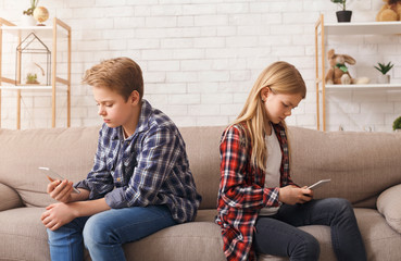 Brother And Sister Using Phones Sitting On Couch At Home