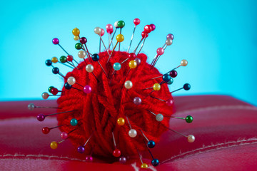 a red skein of thread stuck a lot of needles on red leather on a blue background. close up copy space