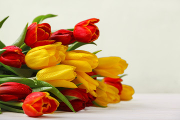 Flowers of spring tulips in dew, on a wooden table. Yellow and red tulips on a beige background. Spring greeting card