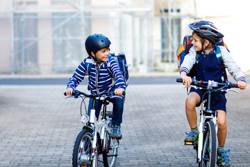 Two school kid boys in safety helmet riding with bike in the city with backpacks. Happy children in...