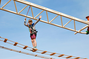 Happy little kid boy climbing on high rope course trail. Active child making adventure and action...