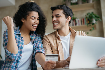 Young happy couple shopping online, sitting at home. Beautiful African American woman holding...