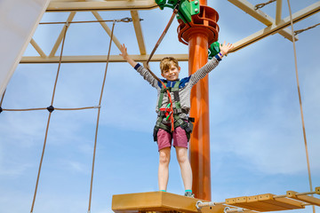 Fototapeta na wymiar Happy little kid boy climbing on high rope course trail. Active child making adventure and action on family vacations. Challenge for brave kids.