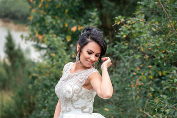 Beautiful slender woman in a long white dress walks in the morning near the lake. girl with long hair walks on the grass in the village, natural cosmetics and makeup