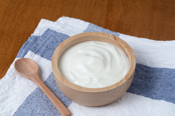 Natural homemade plain organic yogurt in wooden bowl and wood spoon on wood texture background
