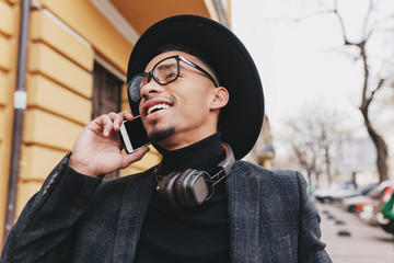 Carefree african guy with short haircut talking on phone with smile. Outdoor photo of enthusiastic...