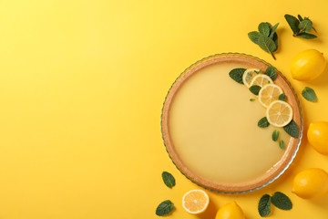 Lemon tart, mint and lemons on yellow background, top view