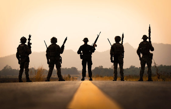 group of military silhouettes on sunset sky background standing on a road