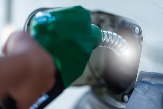Man Handle pumping gasoline fuel nozzle to refuel. Vehicle fueling facility at petrol station. White car at gas station being filled with fuel. Transportation and ownership concept.