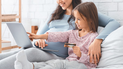Little girl holding credit card, shopping online with mom
