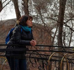 A young girl stands on a bridge in a city park on a weekend, sunny spring day. She enjoys the awakening of nature after winter and the warm sun. Early spring in the city.