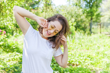 Naklejka na ściany i meble Beautiful young brunete woman with brown hair in trendy yellow sunglasses resting and smiling on park or garden green background. European woman. Portrait of happy teenage girl relaxing outdoor.