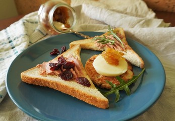 Abundant toast breakfast with pate, cheese and onion marmalade on the blue plate, decorated with dried cranberries and fresh arugula.