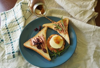A generous toast breakfast with pate, cheese and onion marmalade on a blue plate, decorated with dried cranberries and fresh arugula.