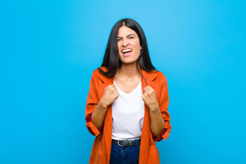 young pretty latin woman shouting aggressively with annoyed, frustrated, angry look and tight...